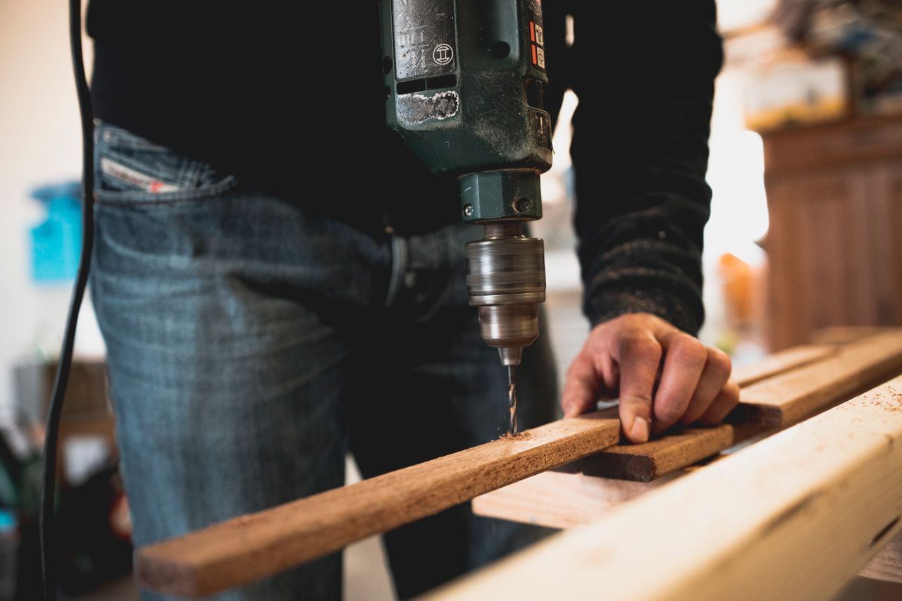 gallery-1 Close-up of a person using an electric drill on a wooden plank, showcasing detailed woodworking skills.