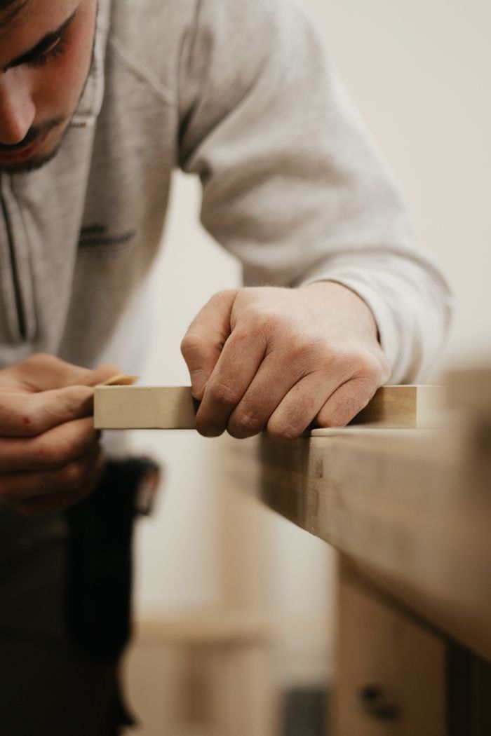 about-01 Close-up of a man meticulously sanding wood, showcasing craftsmanship.