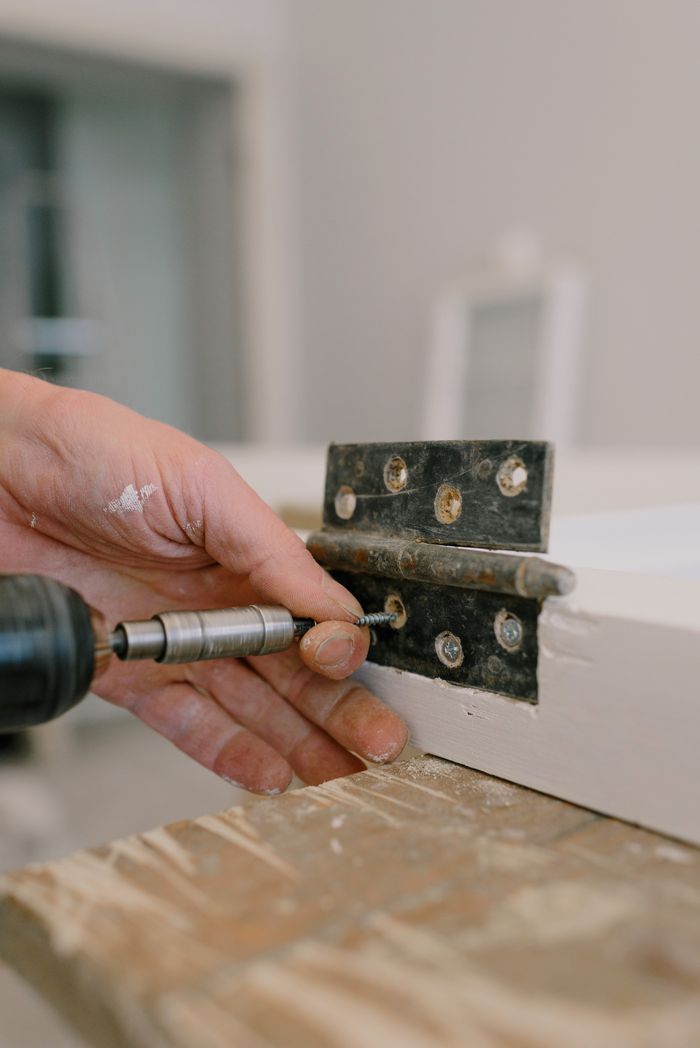 ours-journey Unrecognizable professional male carpenter using screwdriver to attach metal hinge on window in room with blurred background during renovation works