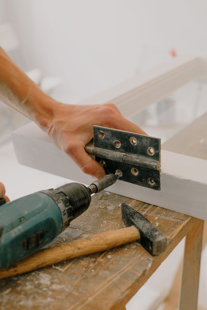 services-01 Crop unrecognizable craftsman attaching metal hinge with modern screwdriver on wooden window frame located on wooden board during renovation works