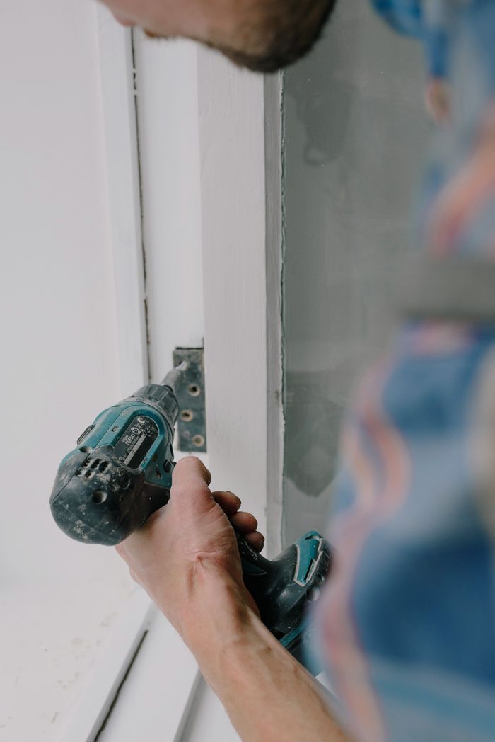 why-choose-us Crop bearded guy installing new wooden window with contemporary screwdriver and metal hinge during renovation process in apartment