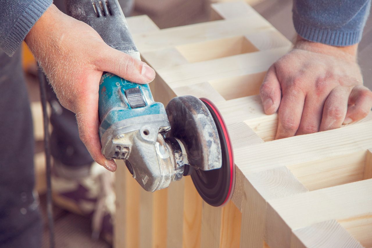 hero-img-01 Crop unrecognizable male carpenter using angle grinder to polish wooden construction in light joinery